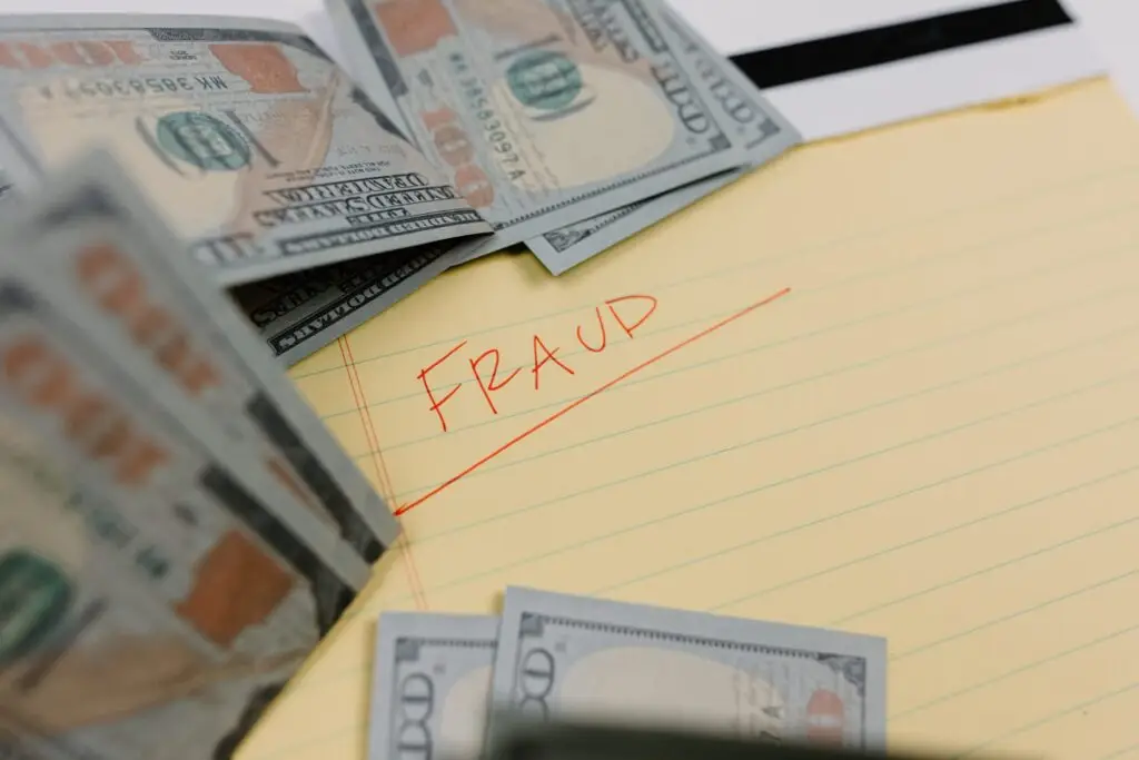 notepad with the word fraud written $100 bills surrounding