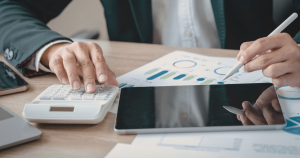 Person using a calculator and stylus while reviewing financial charts